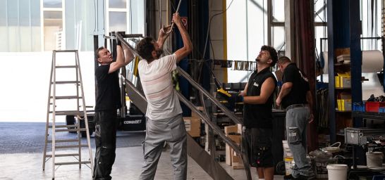 eine Gruppe von Mitarbeitern hängen ein großes Werkstück an die Traverse