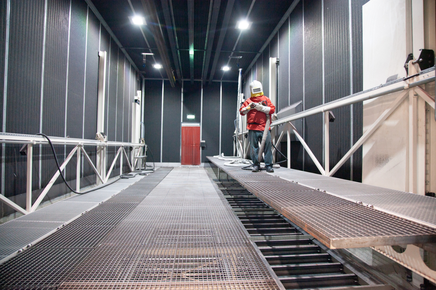 Werker steht mit einer Strhalpistole in einer Strahlkabine eines Kunden